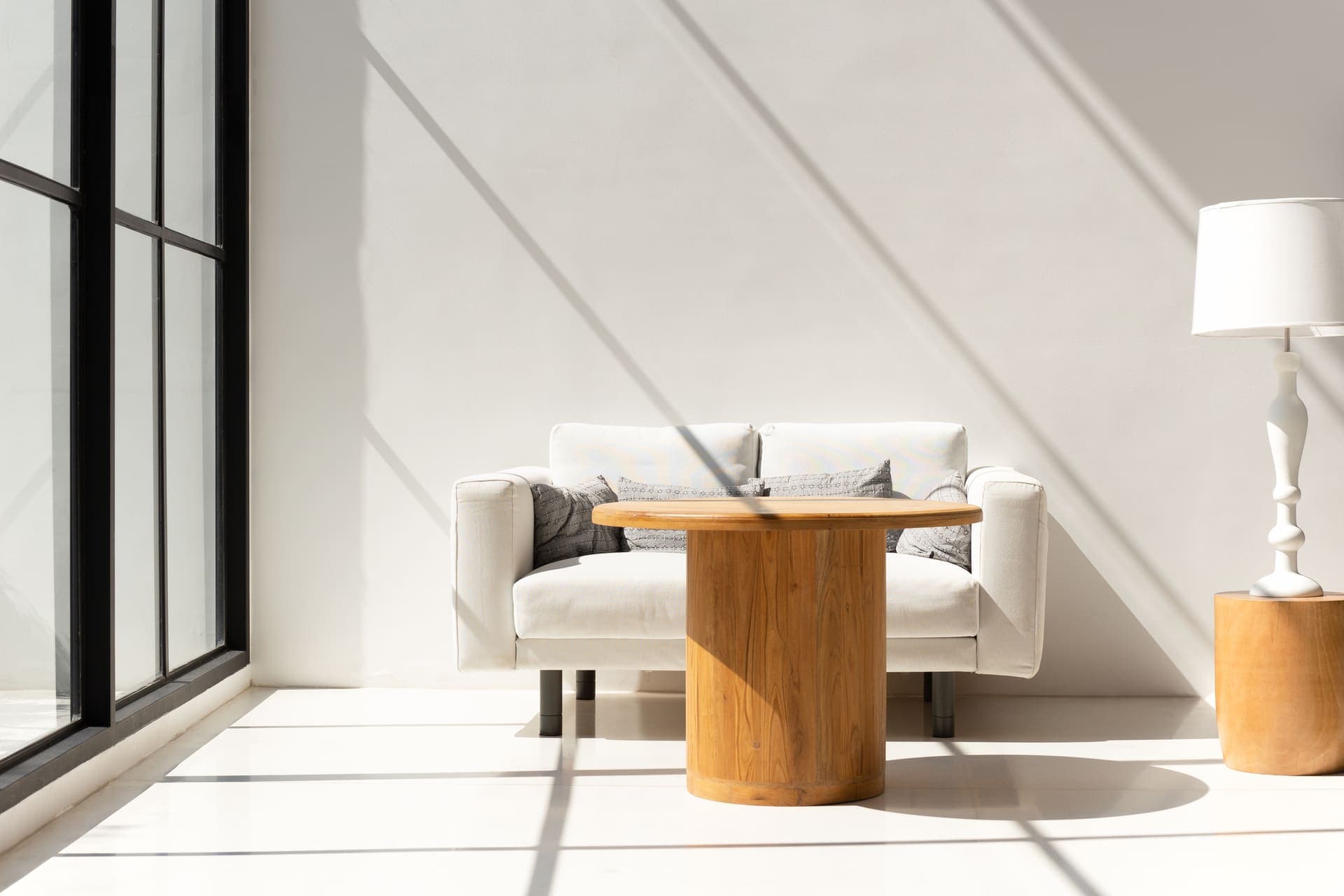 A calm, sunlit living room with a sofa, a wooden table and a lamp
